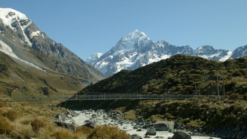 A person crosses a bridge spanning a river in the mountains