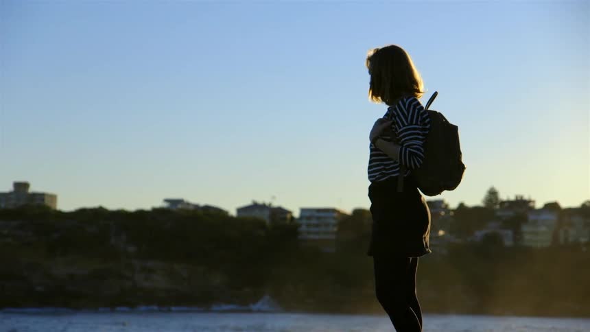 A woman stands by the water at sunset