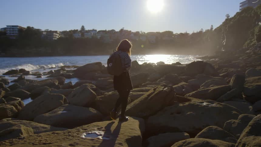 A woman walks over rocks by the shore