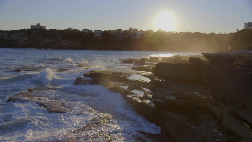 Waves crash against the coast near a town at sunset