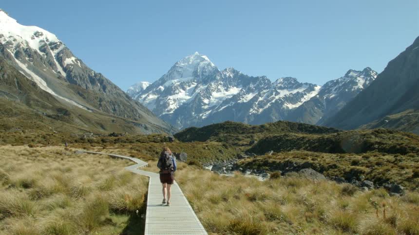 A woman is walking on the boardwalk towards a mountain ahead