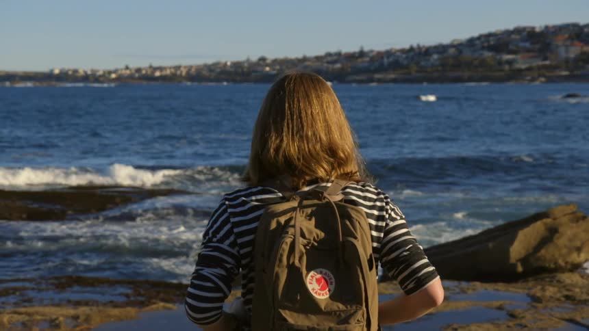 Woman with a backpack looks out over the ocean
