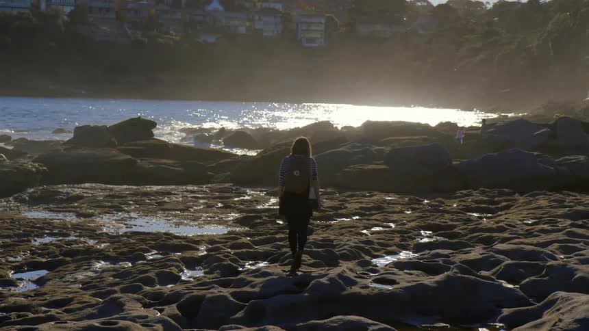 A woman is walking along the rocks by the shore