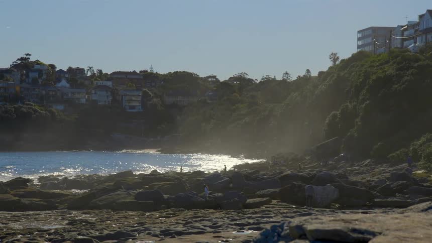 The sun shines down on people on a rocky beach