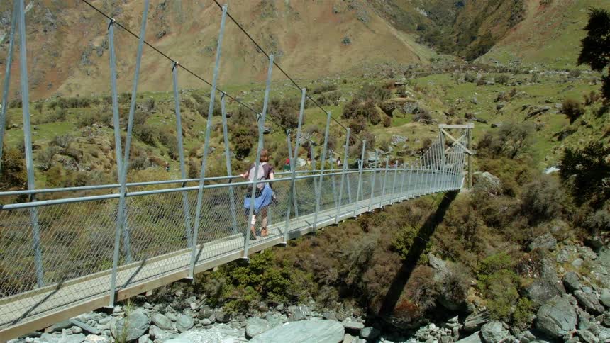 A hiker crosses a long suspension walking bridge