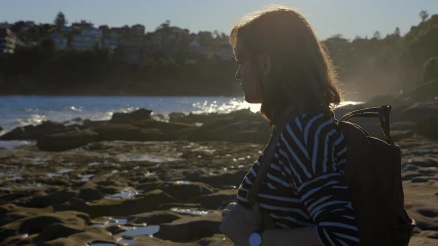 A woman stands near the water watching the waves