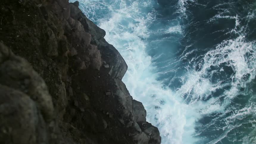 Ocean waves crash at the base of a rocky cliff