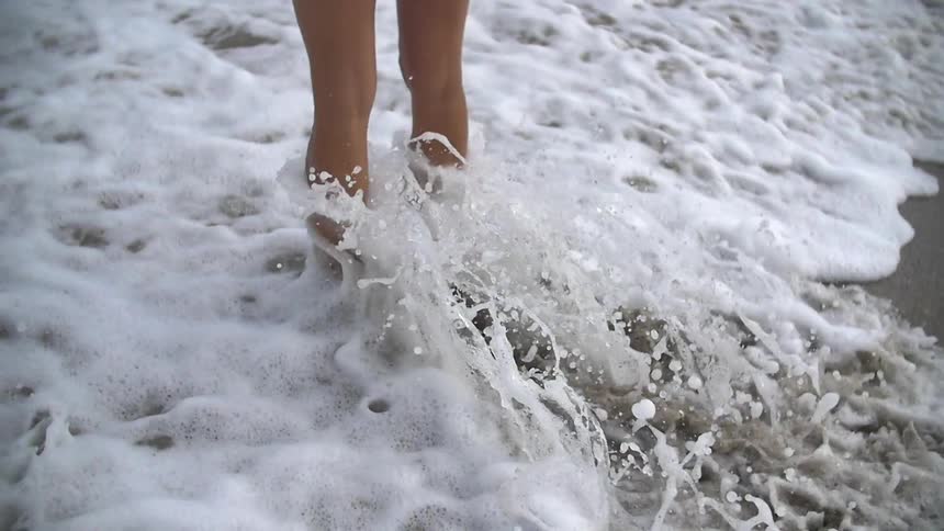 Ocean waves splash around a woman's legs on a sandy beach