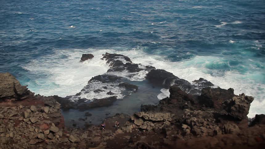 The blue waters crash against the rocks of the shore below
