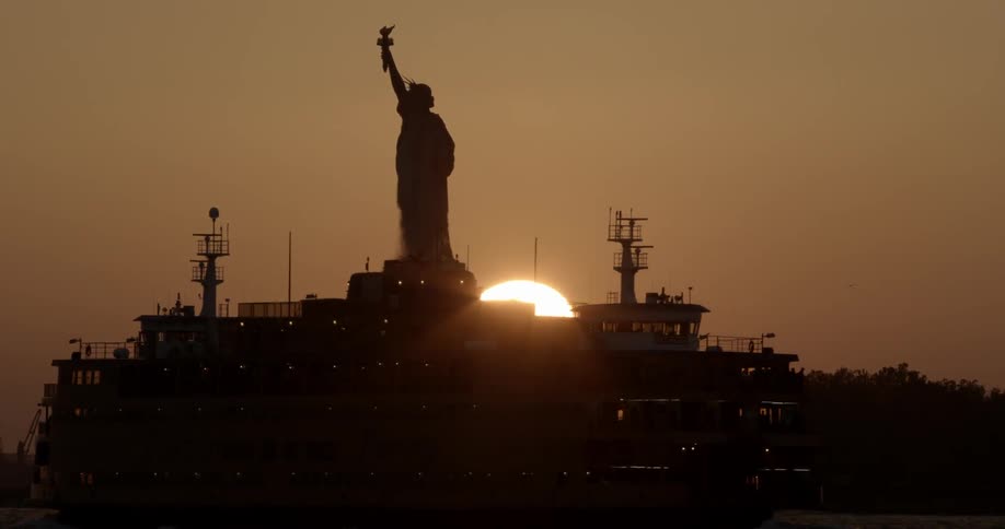 The sun is setting behind the statue of liberty