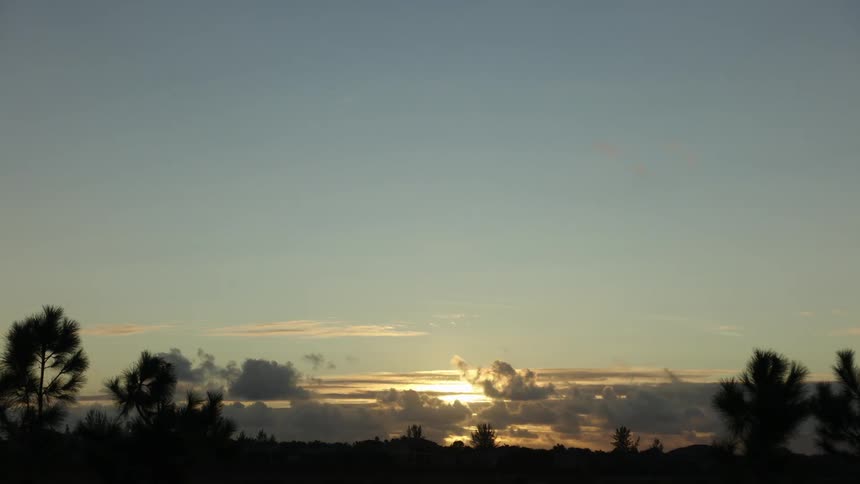 The clouds move across the setting sun in the distance