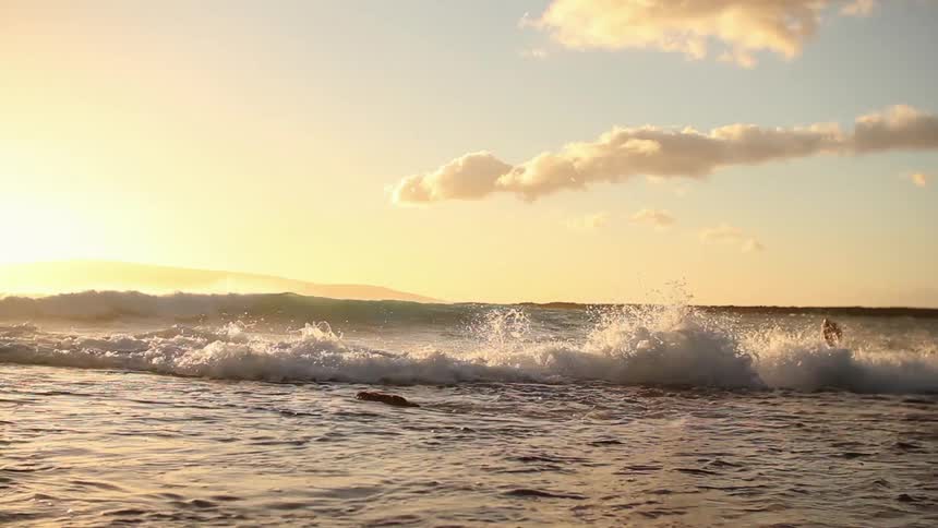The waves crash against the shore at sunset