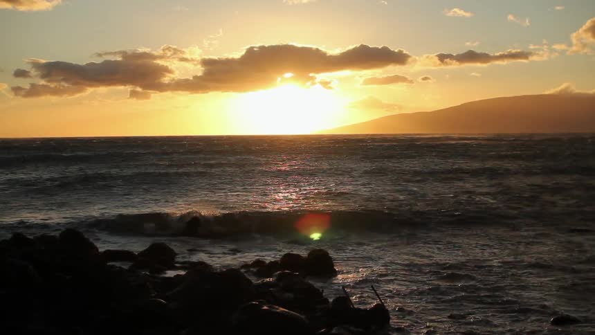 The waves crash against the rocks at sunset