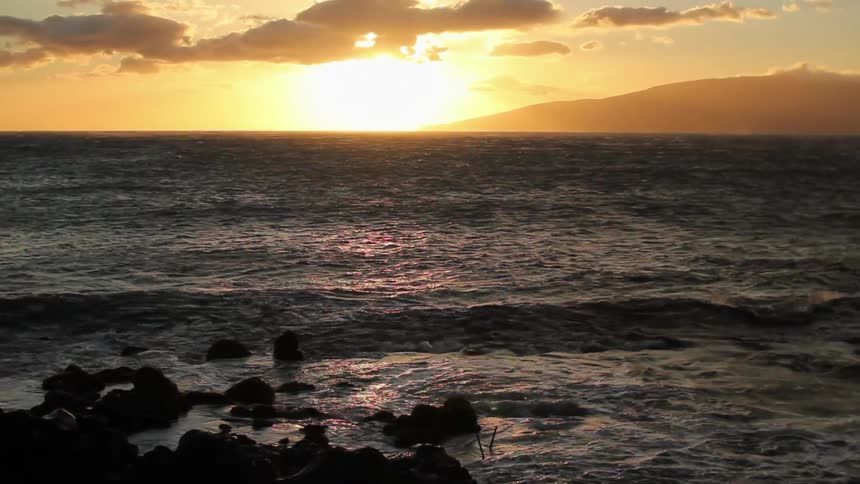 Waves crash against the rocks near the shore at sunset