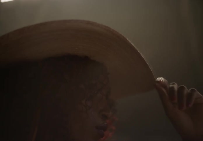 Female model standing in riding arena touches her cowboy hat