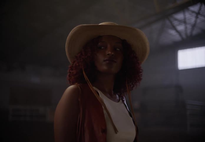 A young woman wearing a cowboy hat and leather vest