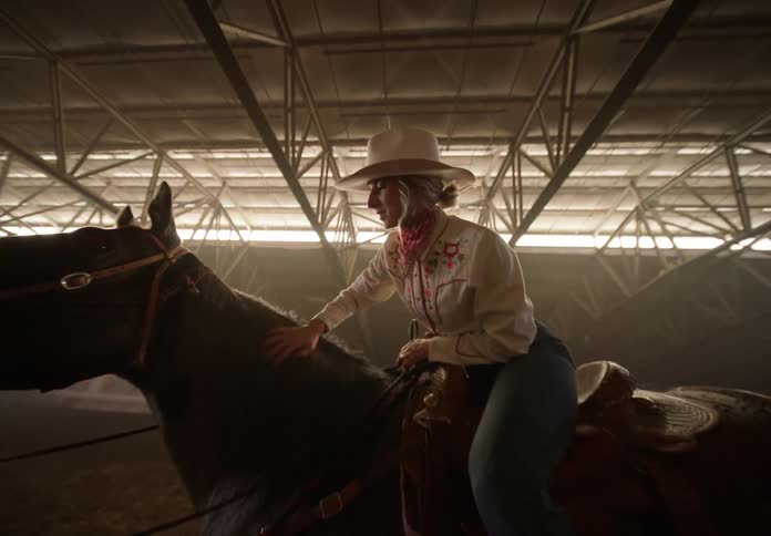 Cowgirl on horseback in a covered arena petting the horse