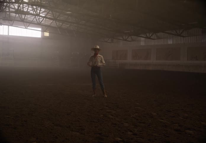 Woman wearing a cowboy hat and cowgirl attire modeling in the arena