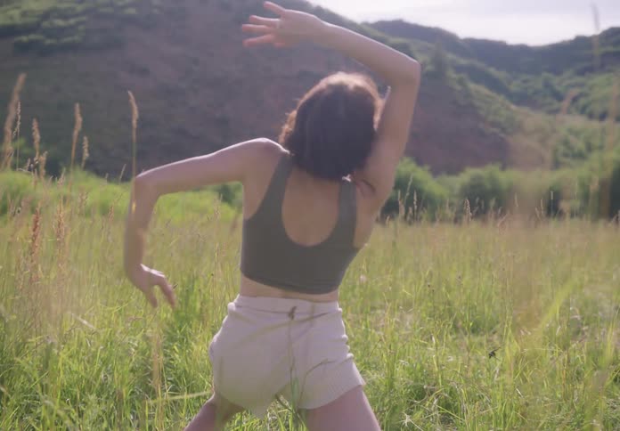 Young thin woman dances stretched on a field of green grass