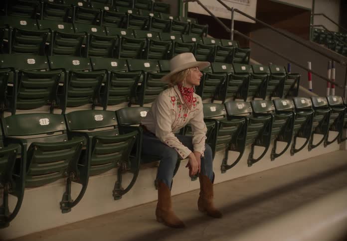 A woman in a stadium wearing cowboy hat and boats seated