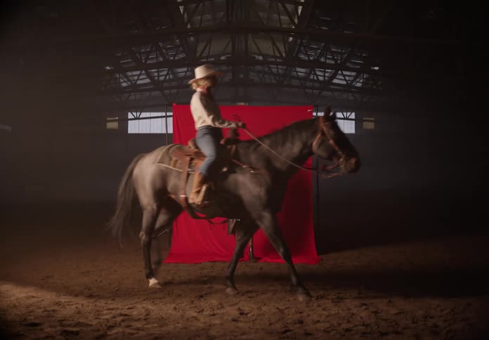 Woman modeling clothes while a cowboy rides a horse