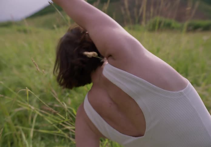 Young woman crouched in a field dancing with her back turned