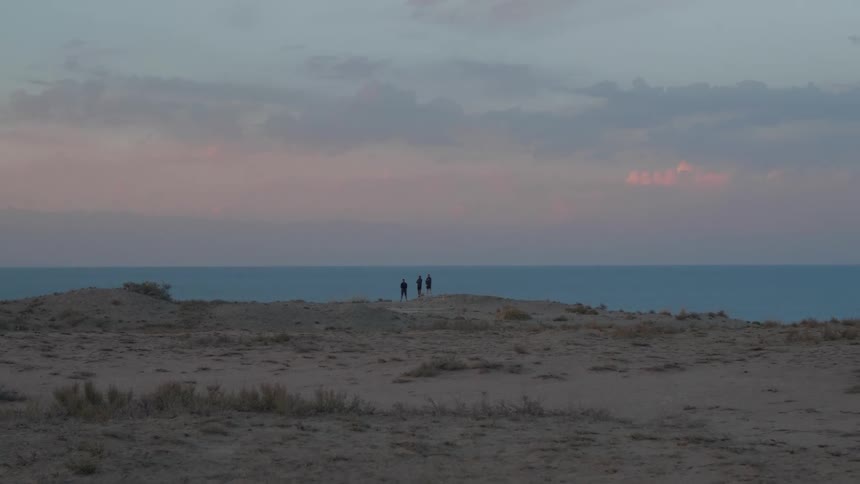 Panoramic view of mountains with three people observing the sea under a morning sky