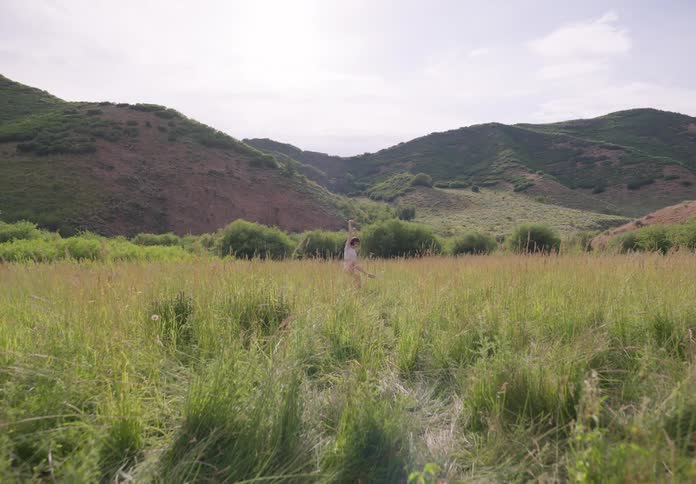 Woman dancing in a field surrounded by a mountain range in daylight