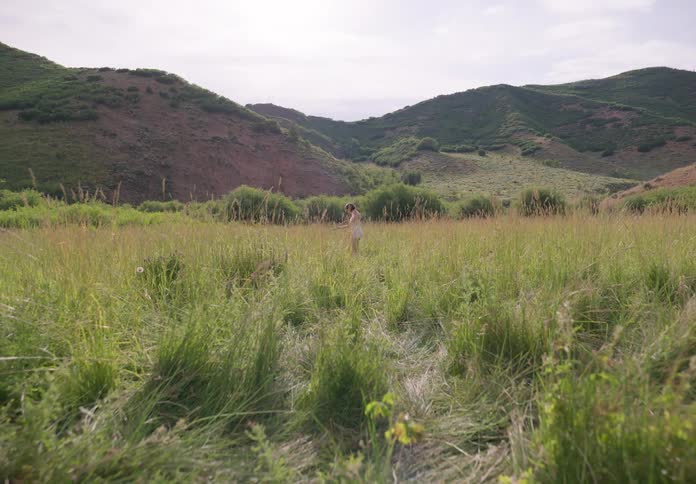 Woman with a bob hairstyle a white shirt and shorts dances on green grass in the field