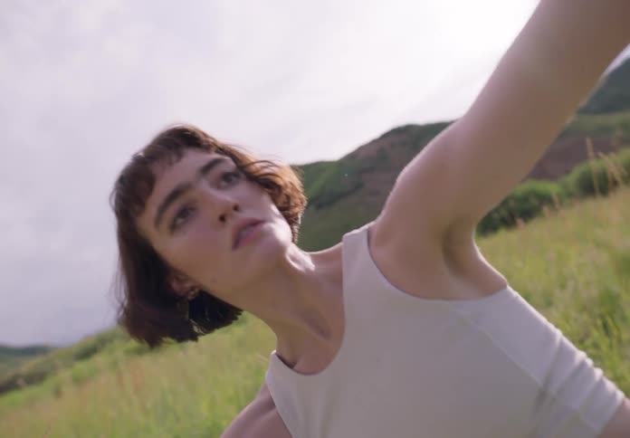 Young thin woman dances stretching on a field of green grass