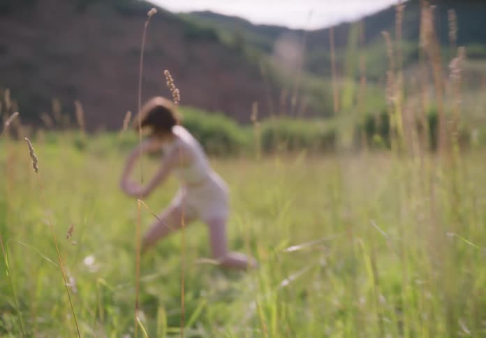 Woman dancing in a grassland with a chain of mountains in the background