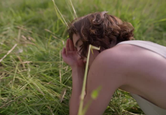 Woman dancing in nature touching her hands and face to leaves in a scenic performance