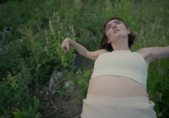 Woman with a bob hairstyle a white shirt and shorts dances on green grass in the field
