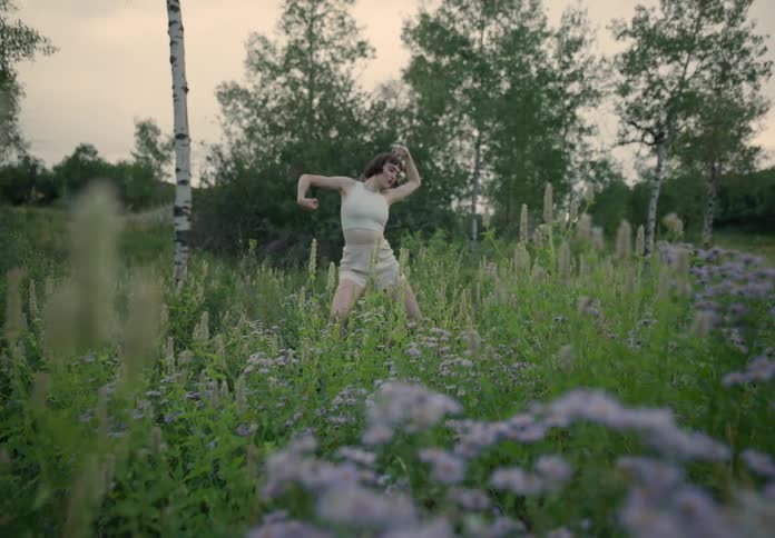 A woman dancing in an open field in nature during sunset