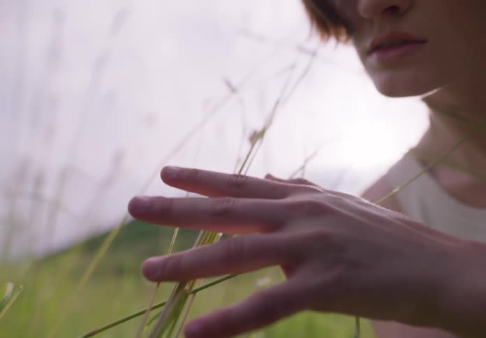 Woman dancing in nature touching hands to leaves in a scenic performance
