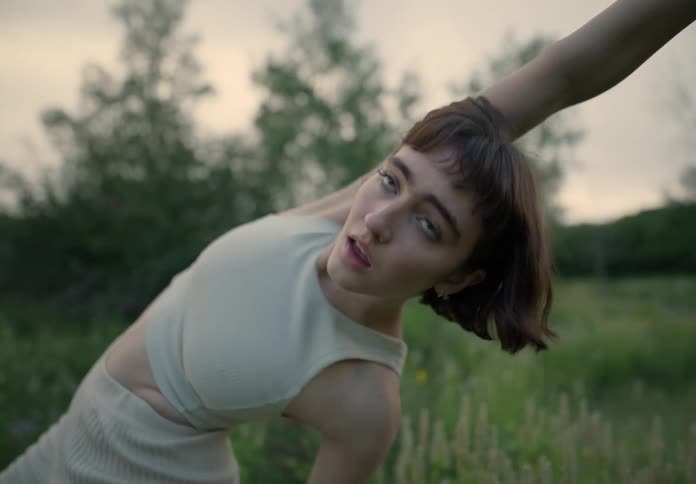 Young thin woman dances stretching on a field of green grass