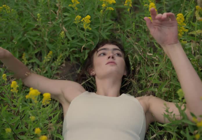 Lady lays on her back in a garden touching flowers during the day