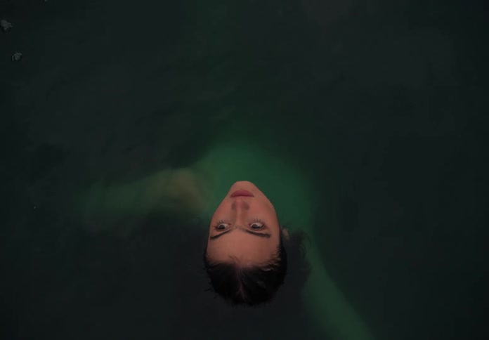 A woman swimming in dark waters contemplating the sky