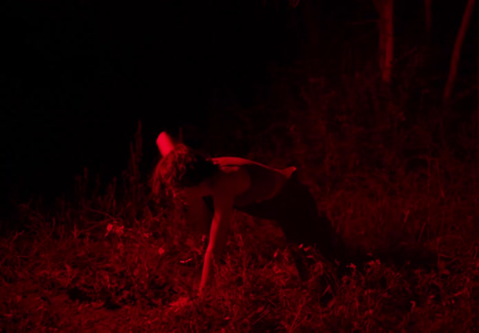 Young thin woman dances stretching on a field under red lights at night