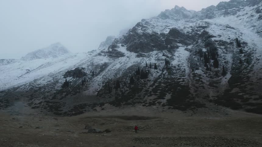 A figure in a red coat approaches a snowcovered mountain