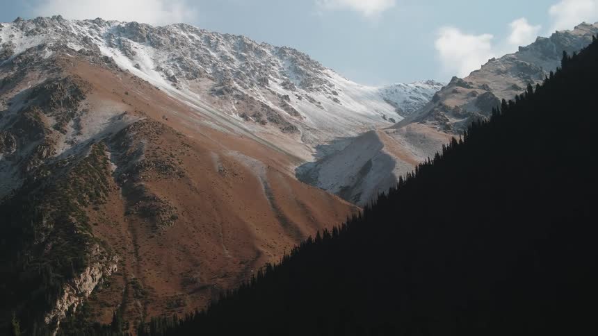 Panorama of a mountain range with coniferous trees some covered in snow in daylight