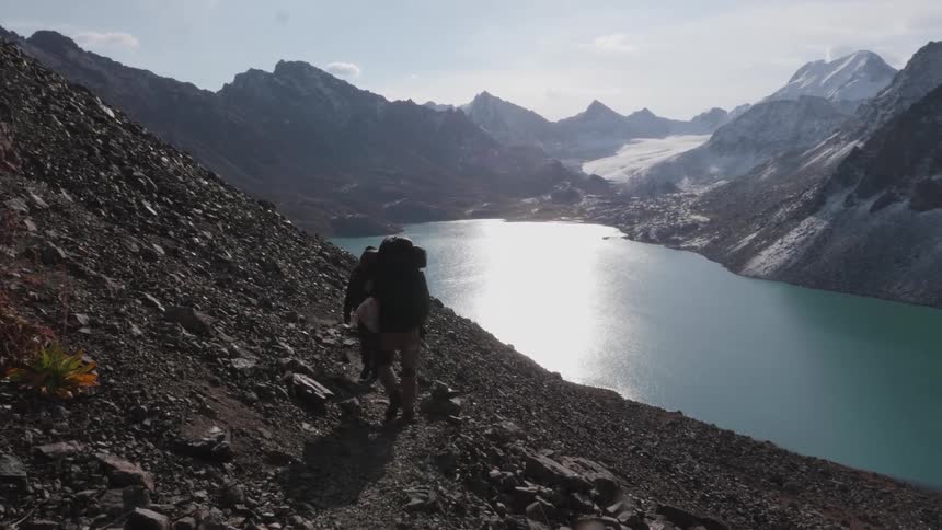 Two people walking on a cliff overlooking a blue lake
