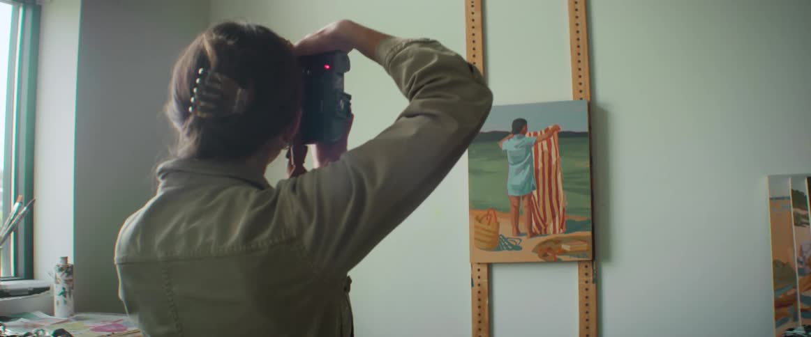 A woman photographer takes photos of a painting representing a person at the beach