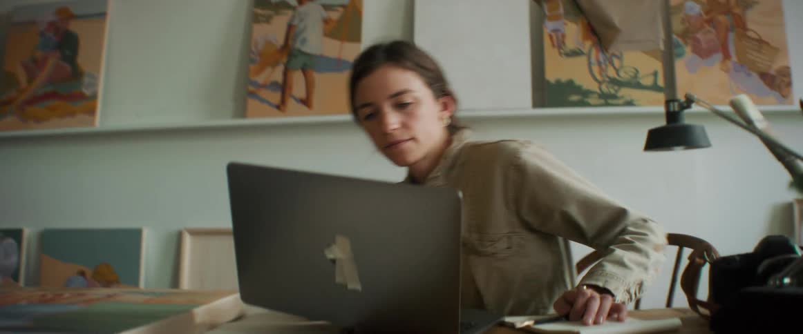 Woman artist sits at a table using a silver laptop for her creative work
