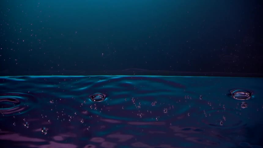 Droplets falling into neon water and forming bubbles in slow motion