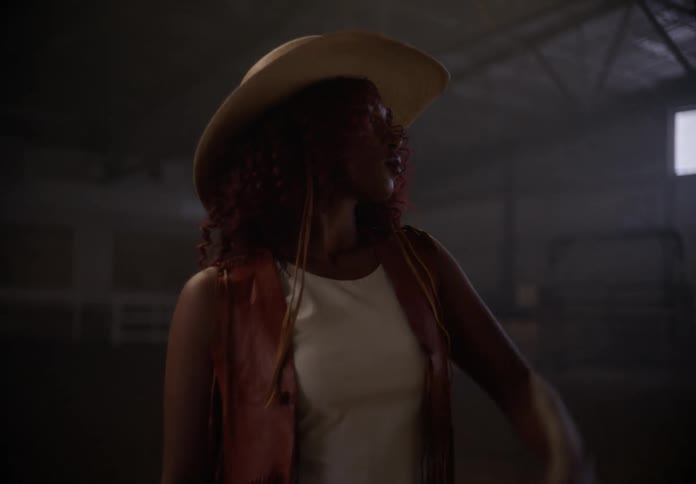 Lady touches her hat while standing in a barn