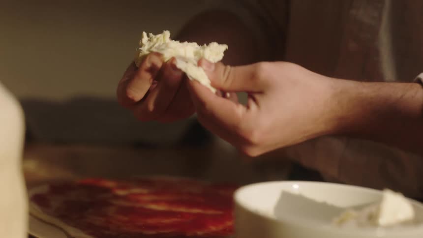 Closeup of a persons hands putting ingredients on a pizza dough