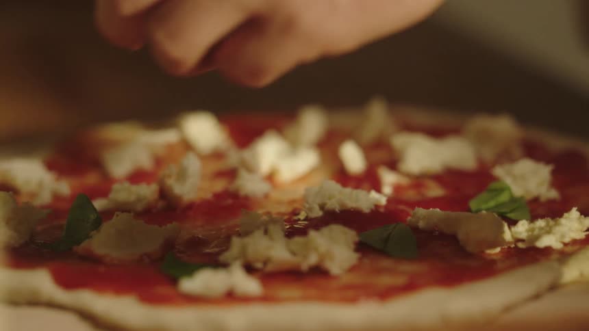 Man puts fresh mozzarella and herbs on a pizza