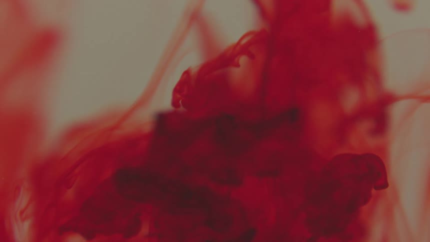 Red paint dripping under water and dissolving in slow motion