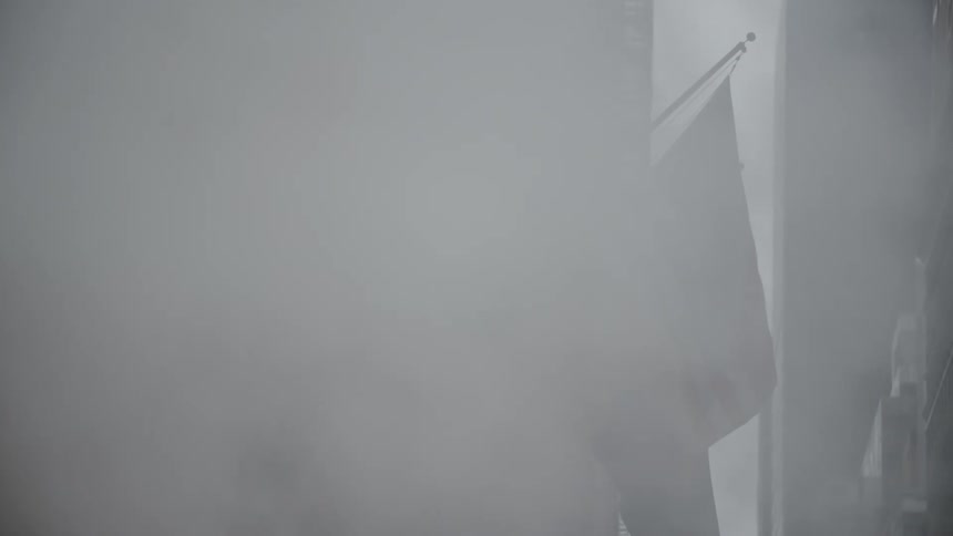 Country flags hanging on poles outside a building obscured by smoke from the street below